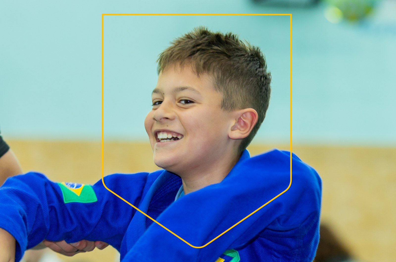Young student in a blue gi smiling during a kids Jiu Jitsu class in Doha